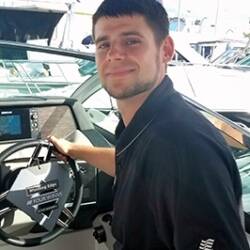 Josh Buck smiles from the wheel of a boat.